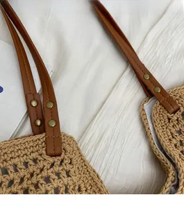 Detail of woven straw tote bag with reinforced brown leather handles and gold rivets