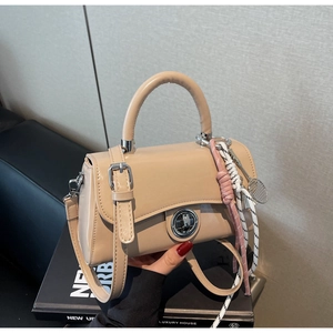 Detail van beige laks leren tas met zilveren draaisluiting en tennisbedeltje