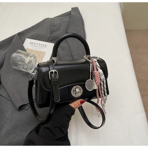 Detail van zwarte glanzende lederen crossbodytas met zilveren sluiting en tennisbedeltje