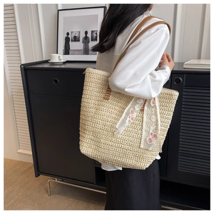 Dettaglio della borsa tote in paglia intrecciata con manici in pelle e nastro di pizzo