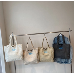 Detail of canvas tote bags with bow embroidery in white, beige, khaki, and dark grey