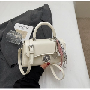 Detail van de gebroken witte leren tas met metalen draaisluiting en geweven hanger accessoire