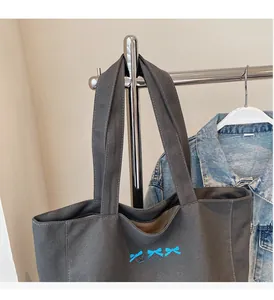 Detail of dark grey canvas tote bag featuring blue bows and a secure zipper closure