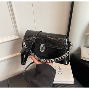 Detail of a black wrinkled patent leather handbag with a silver chunky chain and flap buckle