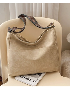 Large beige tote bag with vintage jacquard strap on white chair in soft light