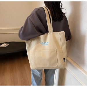 Detailed view of canvas tote bag with blue bow embroidery and side functional pocket