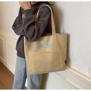 Close-up of beige canvas tote bag with blue bow accents and shoulder strap on model