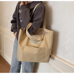 Detailed shot of beige canvas tote bag with blue bow graphic and large front pocket