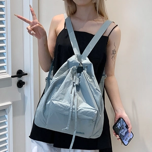 Detail of light blue drawstring backpack showing textured fabric and front zipper pocket