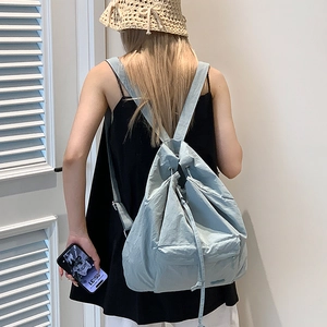 Detail of light blue drawstring backpack showing pleated texture and front zipper pocket
