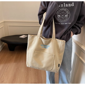 Detail of off-white canvas tote bag featuring blue bow print and front pocket