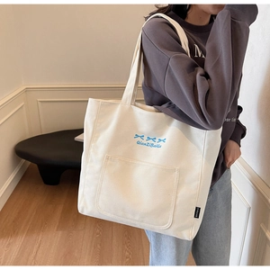Detail of white canvas tote bag featuring blue bow embroidery and spacious front pocket