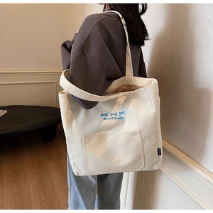 Detail of a cream canvas tote bag featuring blue bows and a functional front pocket