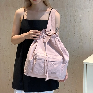 Detail of light pink drawstring canvas backpack featuring wide straps and front zipper pocket