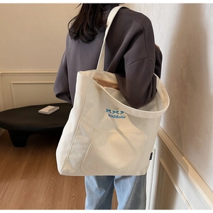 Detailed side view of white canvas tote bag with blue bow embroidery and large side pocket