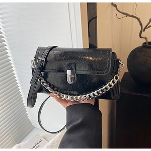 Close-up of black glossy crossbody bag with silver chain and vintage crackle texture
