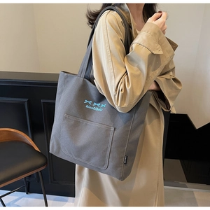Detailed view of dark grey canvas tote bag with blue bow embroidery and side label