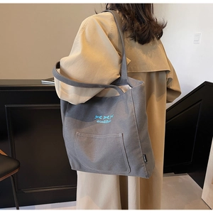 Detail of grey canvas tote bag with blue bow embroidery and front pocket feature