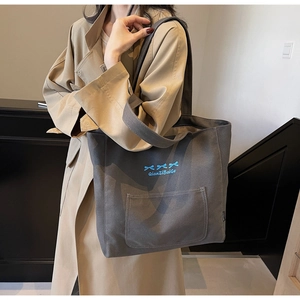 Detailed view of dark grey canvas tote bag with blue bow embroidery and strap