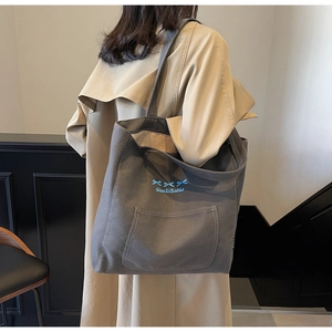 Detail of dark grey canvas tote bag with blue bow embroidery and side pocket detail