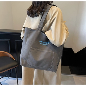 Close-up of grey canvas tote bag with blue bow embroidery and side woven label detail