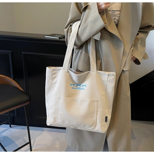Close-up of beige canvas tote bag with blue bow embroidery and front pocket detail