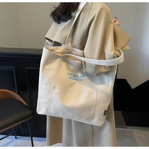 Detail of a beige canvas tote bag with blue bows and a functional front pocket on the model