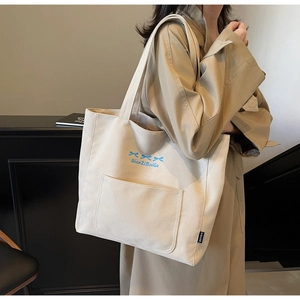 Close-up of beige canvas tote bag with blue bow embroidery worn with a khaki trench coat