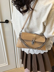Beige patent leather crossbody bag with silver chain worn by model in minimalist room