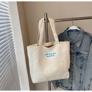 Detail of off-white canvas tote bag featuring blue bow print and large front pocket
