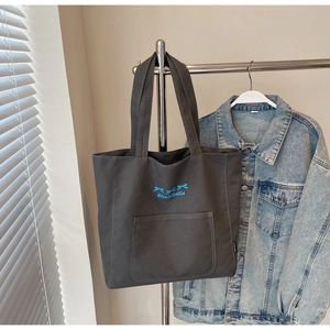 Detail of dark grey canvas tote bag with blue bow embroidery and front outer pocket