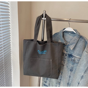 Close-up of charcoal canvas tote bag featuring blue bow embroidery and front pocket