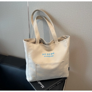 Close-up of beige canvas tote bag with light blue bow embroidery and side woven label