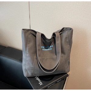Close-up of dark grey canvas tote bag with blue bow embroidery and front pocket detail