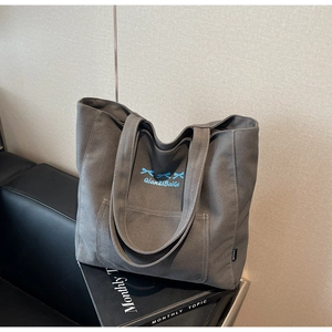 Detailed macro view of dark grey canvas tote with blue bow embroidery and side pockets