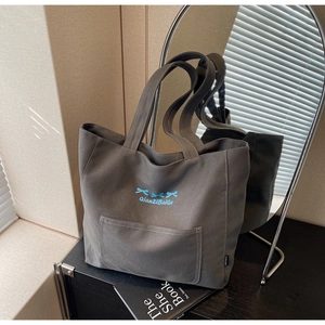 Detail of grey canvas tote bag with blue bow embroidery on a stylish shelf display