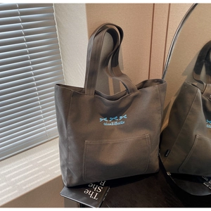 Detail of dark grey canvas tote bag with blue ribbon bows and embroidered text on front