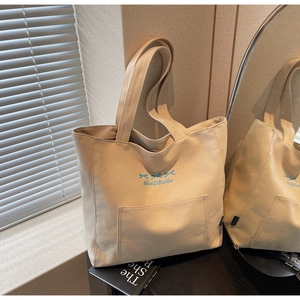 Detail of canvas tote bag with blue bow embroidery and side pocket in home setting