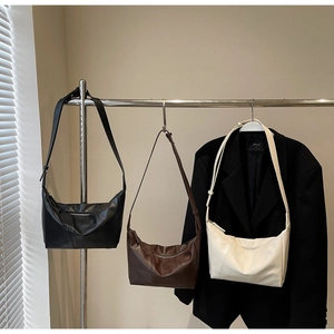 Three minimalist half-moon crossbody bags in black, coffee, and white on a display stand