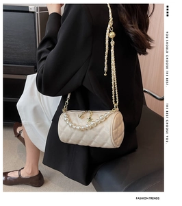 Close-up of cream cylinder bag featuring quilted stitching and pearl chain strap