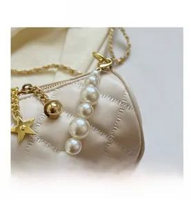 Detail of beige quilted cylinder bag with pearl handle and gold star charm detail