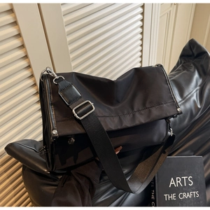 Detail of black nylon messenger bag with wide shoulder strap and silver metal hardware