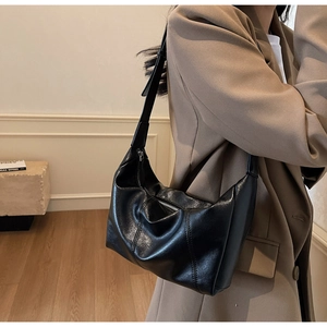 Detail of black leather shoulder bag with silver zipper and adjustable strap on model