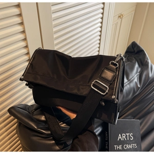 Detail of black nylon crossbody bag featuring silver metal buckle and wide shoulder strap