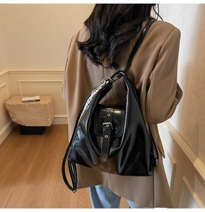 Détail d'un sac hobo en cuir verni noir avec boucle argentée et foulard à carreaux sur mannequin