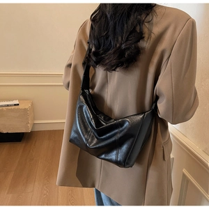 Detail of black leather half-moon shoulder bag with visible stitching and adjustable strap