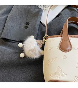 Close-up of cream leather bucket bag with embossed butterfly and white plush charm
