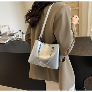 Detail der silbernen Metallic-Eimertasche mit Kettenriemen in einem modernen Café