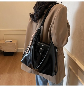 Détail d'un grand sac cabas en cuir verni noir avec boucle et pompon rose sur modèle