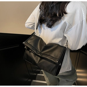 Close-up of black litchi pattern leather texture with silver rivets on a crossbody bag